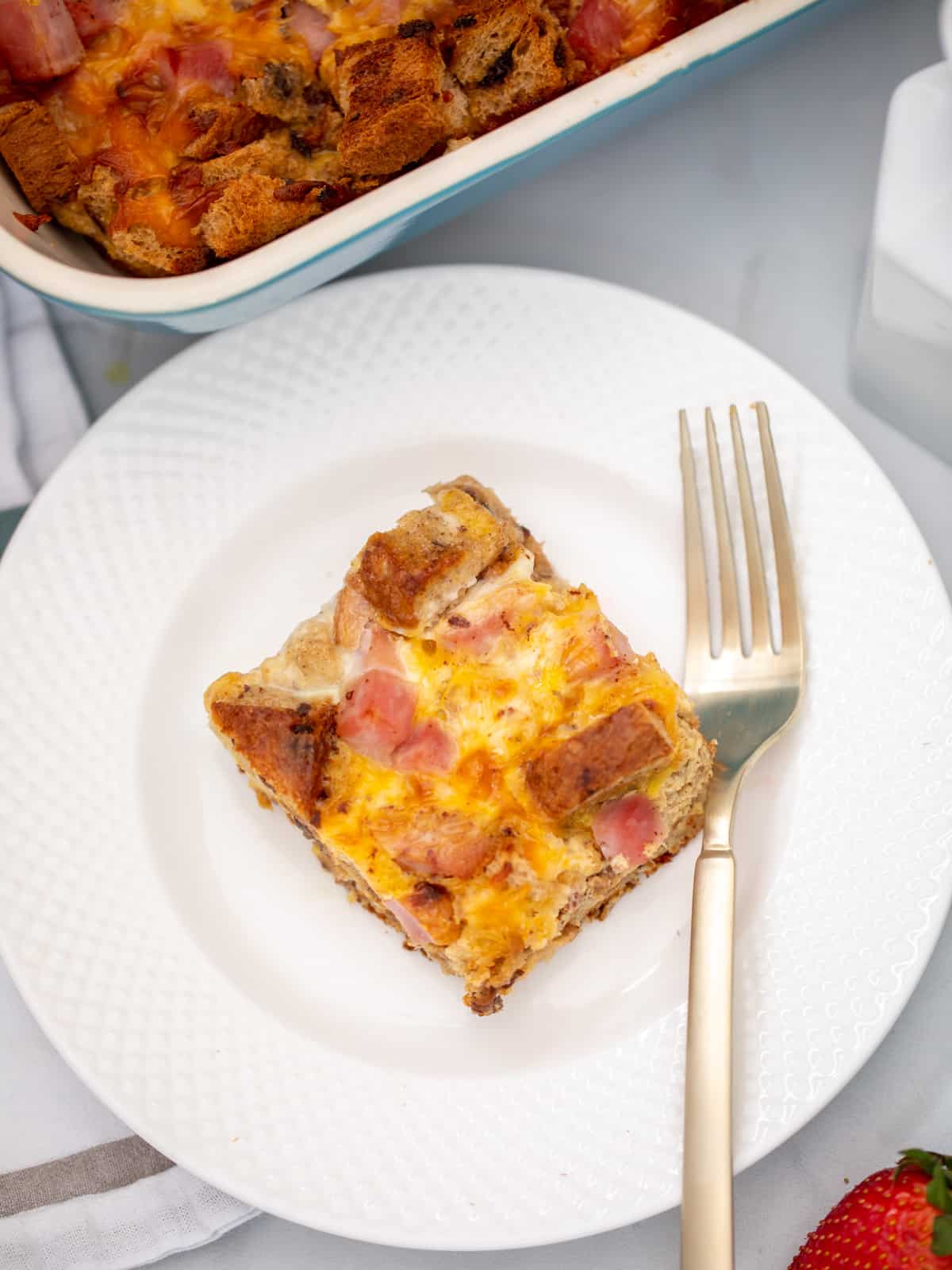 Slice of ham and egg breakfast casserole on white plate with fork next to it. 