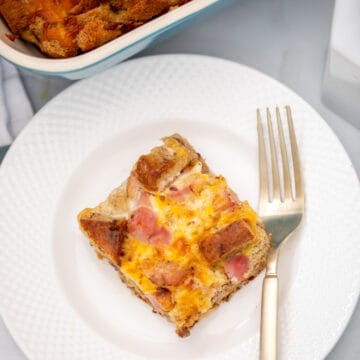 Slice of ham and cheese breakfast casserole on white plate next to fork.
