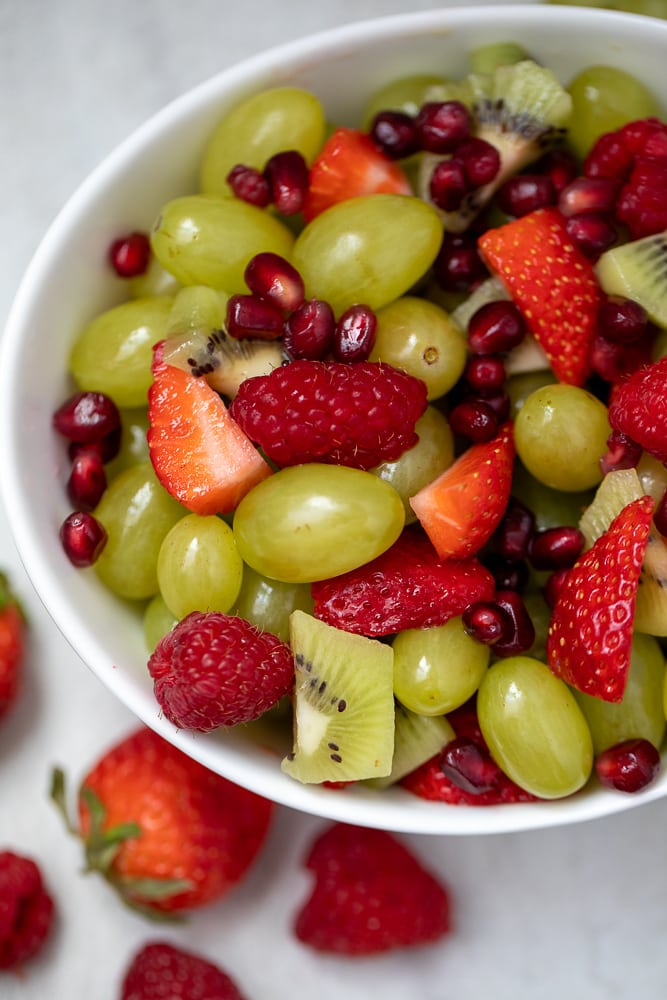 Red and green fruit tossed in a white serving bowl