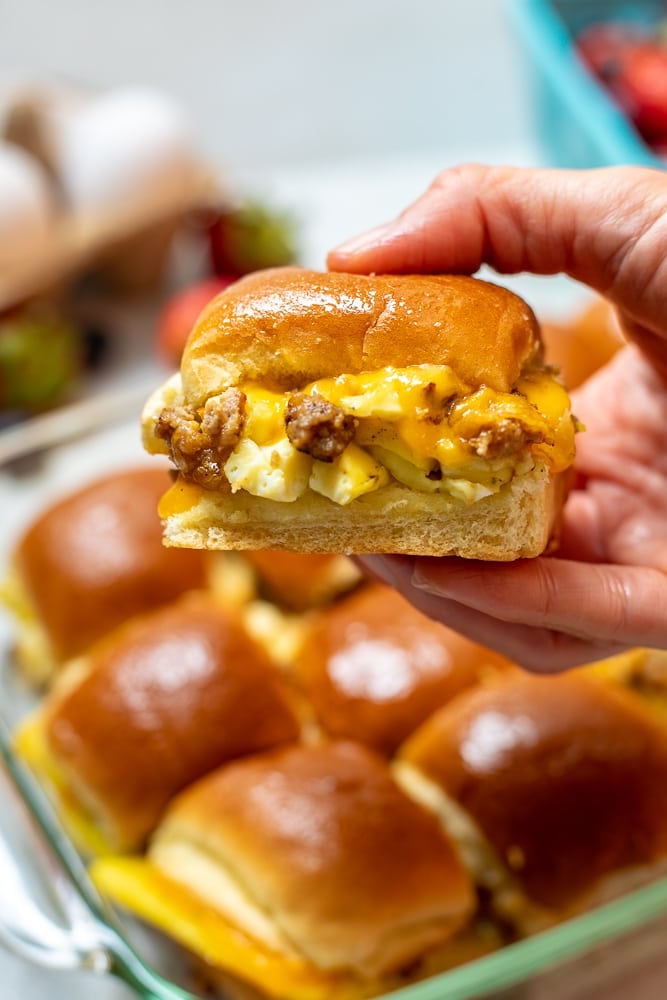 Hand holding breakfast slider with sausage, eggs, and cheese.