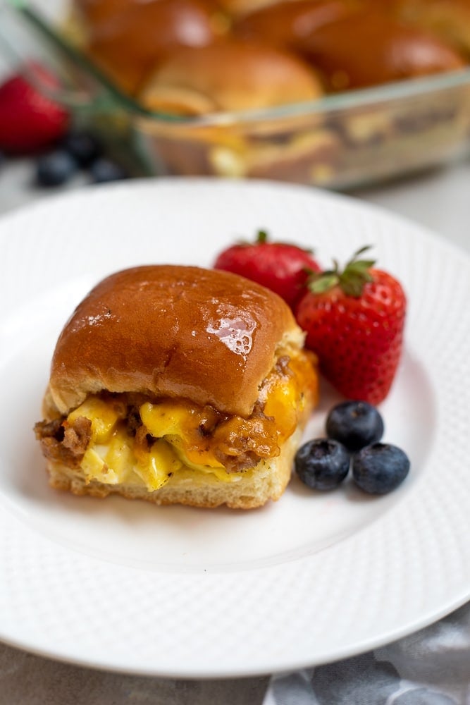 Breakfast Slider with eggs, sausage, cheese on white plate with fruit