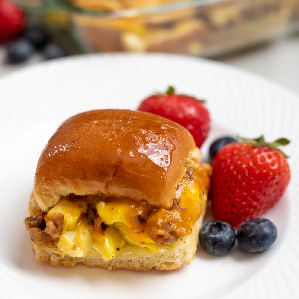 Breakfast Slider with eggs, sausage, cheese on white plate with fruit