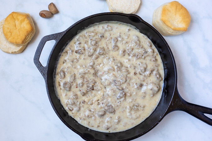 Cast Iron Skillet with sausage gravy next to biscuits.