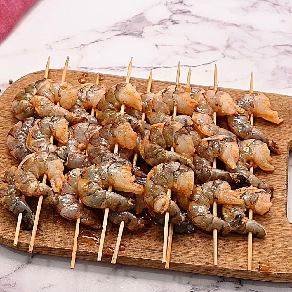 Skewered marinated shrimp on wooden cutting board.