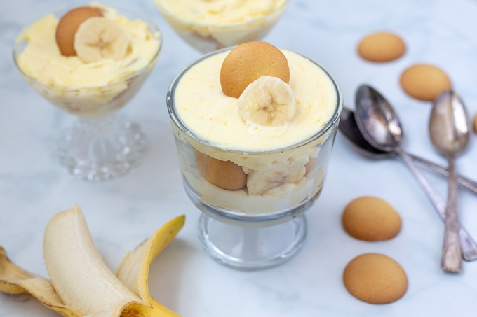 Banana Pudding layered in 3 mini trifle dishes next to bananas and vanilla wafter.