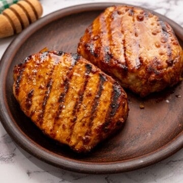 Grilled Pork Chops on wooden platter next to honey.