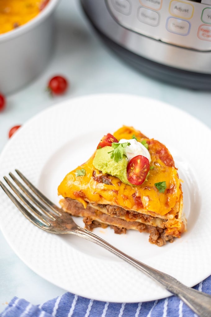 Slice of Instant Pot Mexican Lasagna on white plate with Instant Pot in background.