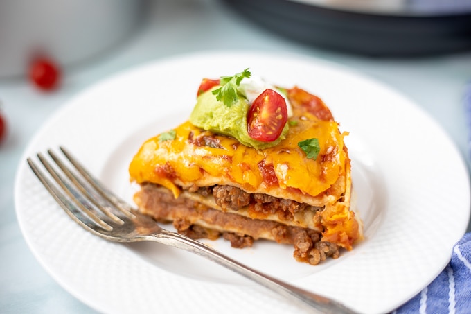 Slice of Mexican Lasagna on white plate topped with tomato and guacamole.