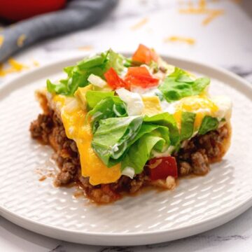 Slice of Mexican Lasagna on white plate topped with tomatoe, onion, and lettuce