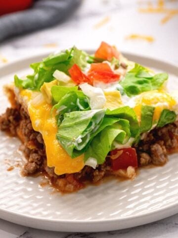 Slice of Mexican Lasagna on white plate topped with tomatoe, onion, and lettuce