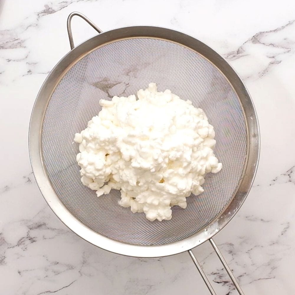 Cottage cheese in strainer over bowl.