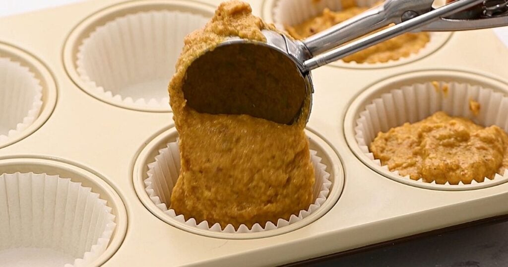 Ice scream scoop scooping muffin batter into muffin tin.