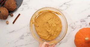 Pumpkin muffin batter mixed together in clear mixing bowl.