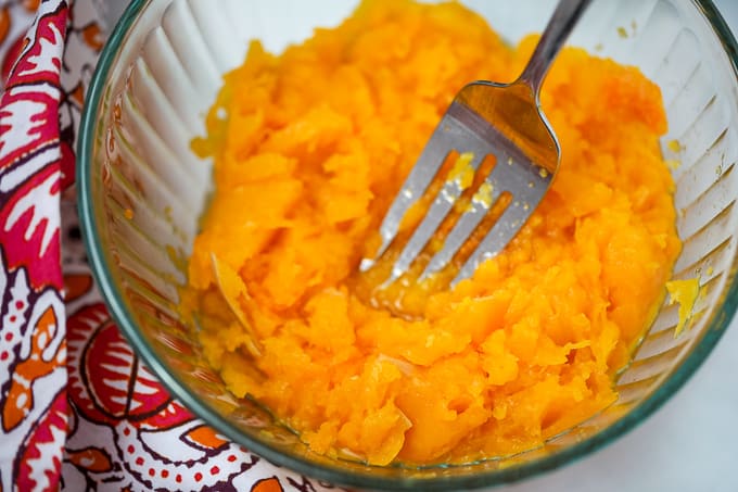 Butternut Squash being mashed with a fork in a glass bowl.