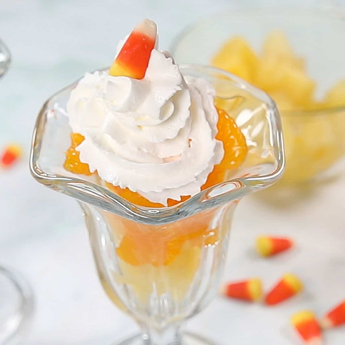 Layered fruit in glass parfait dish topped with candy corn.