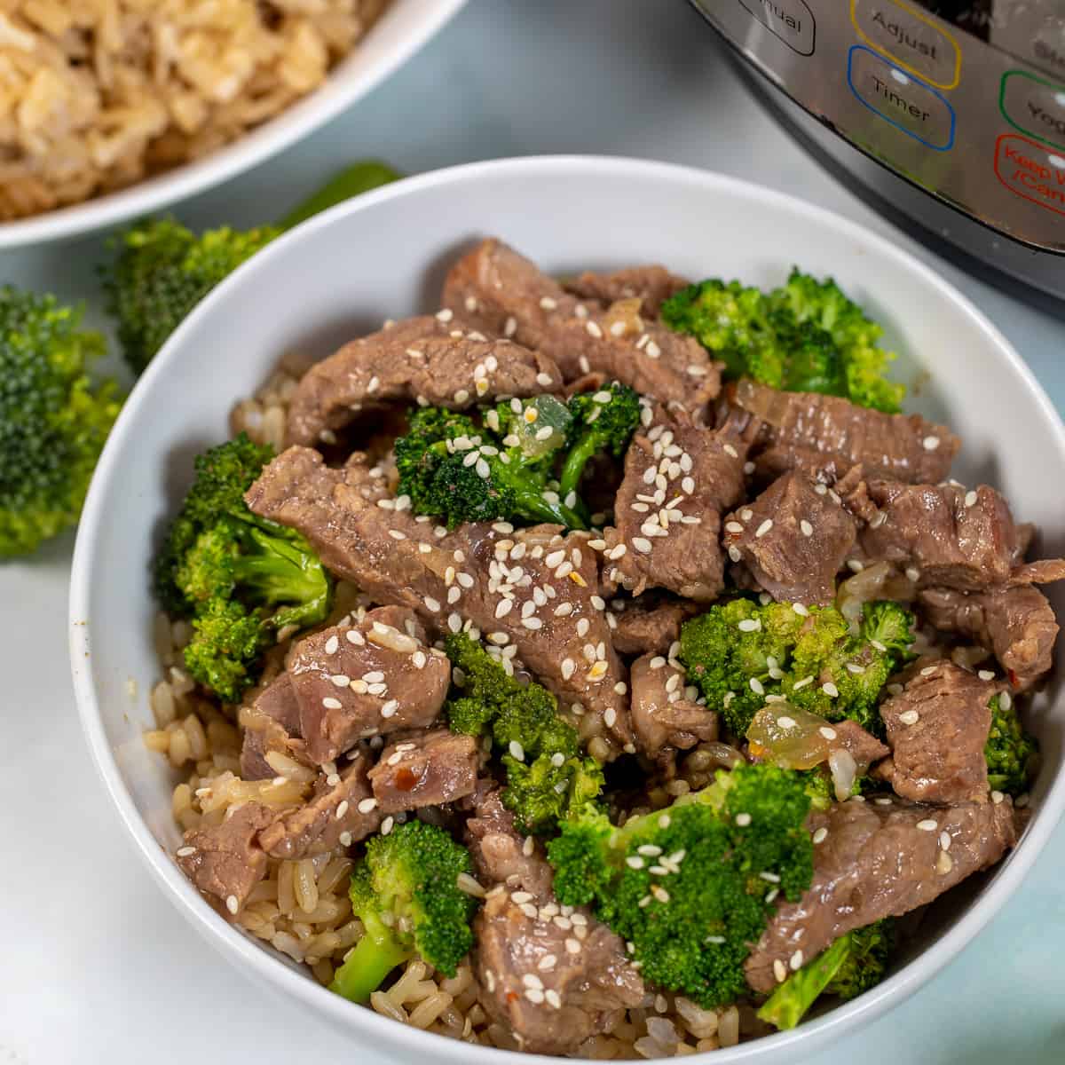 Beef and Broccoli in white bowl topped with sesaame seeds.