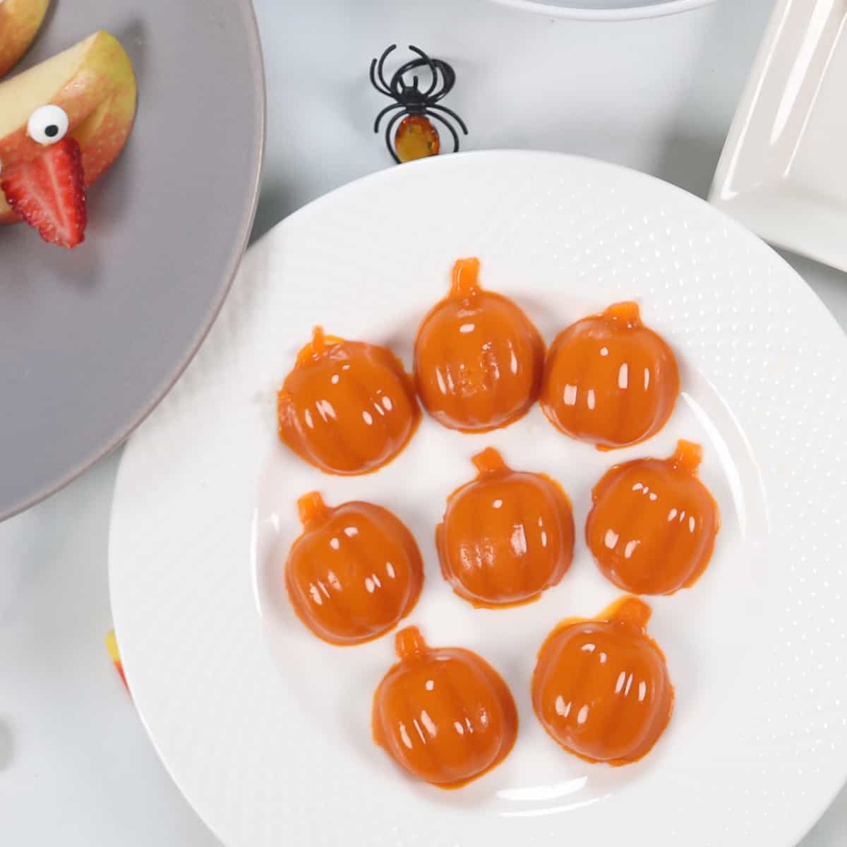 Pumpkin shaped gummies on a white plate. 