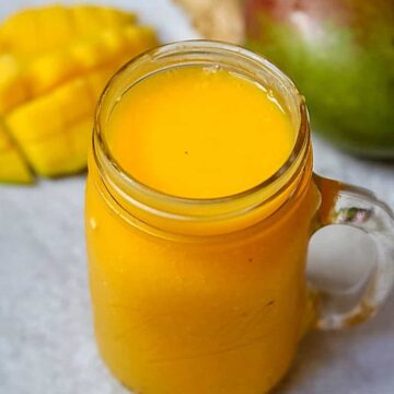 Glass of mango smoothie next to fresh mango.