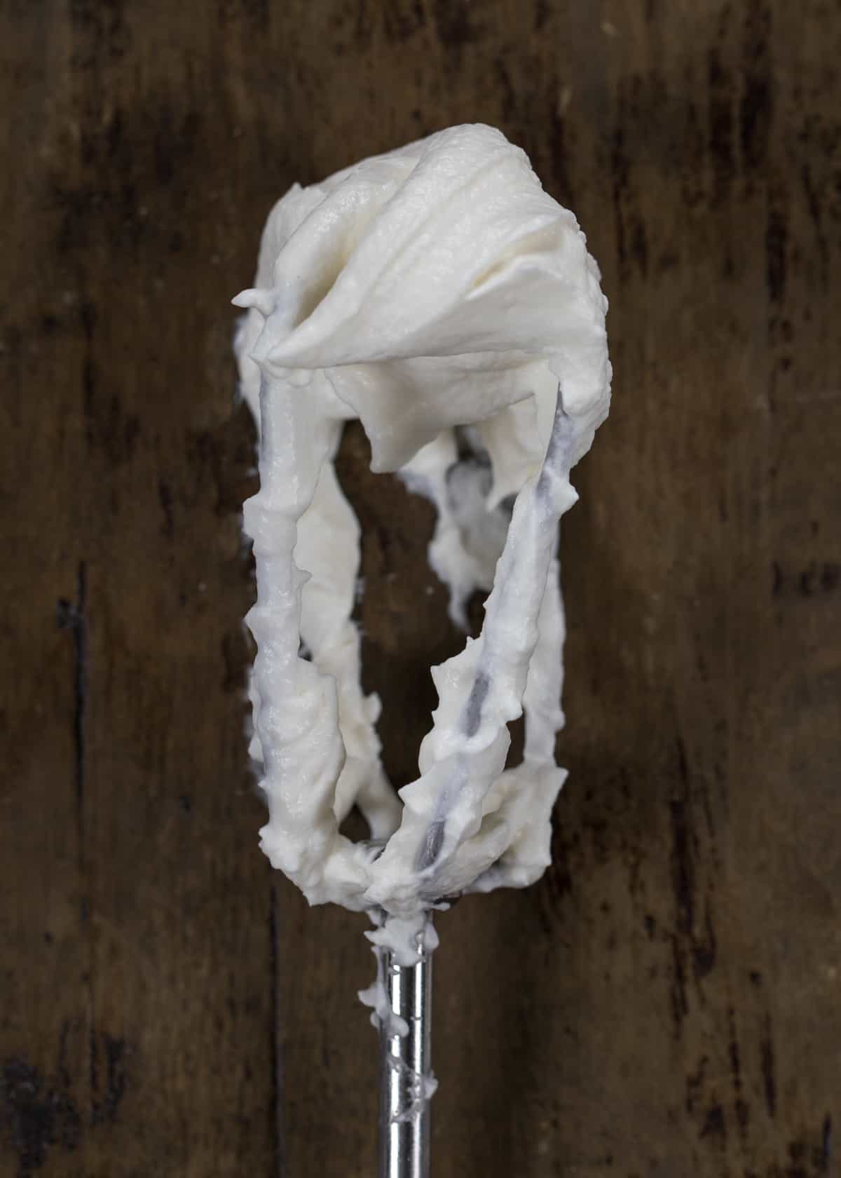 Beater with whipped cream with soft peaks on it.
