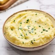 Bowl of creamy mashed potatoes topped with butter and chives.