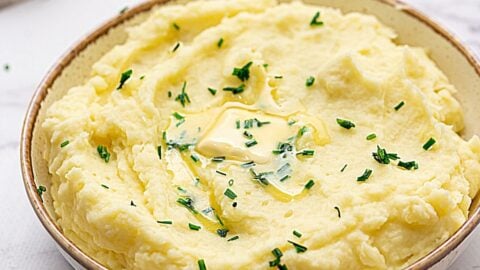 Bowl of creamy mashed potatoes topped with butter and chives.
