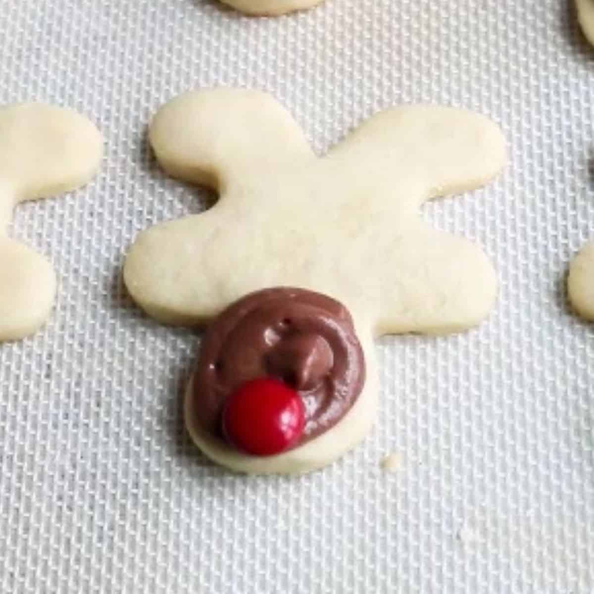 Reindeer cookie with red m&m nose on baking mat.