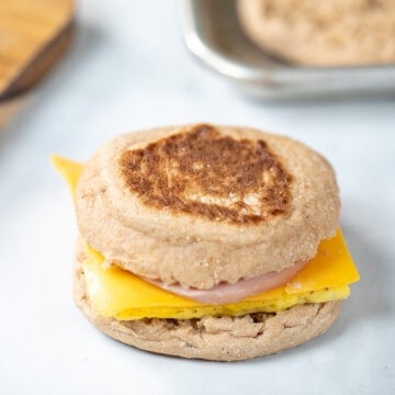 A copycat egg mcmuffin breakfast sandwich on counter with toasted English muffins in background.