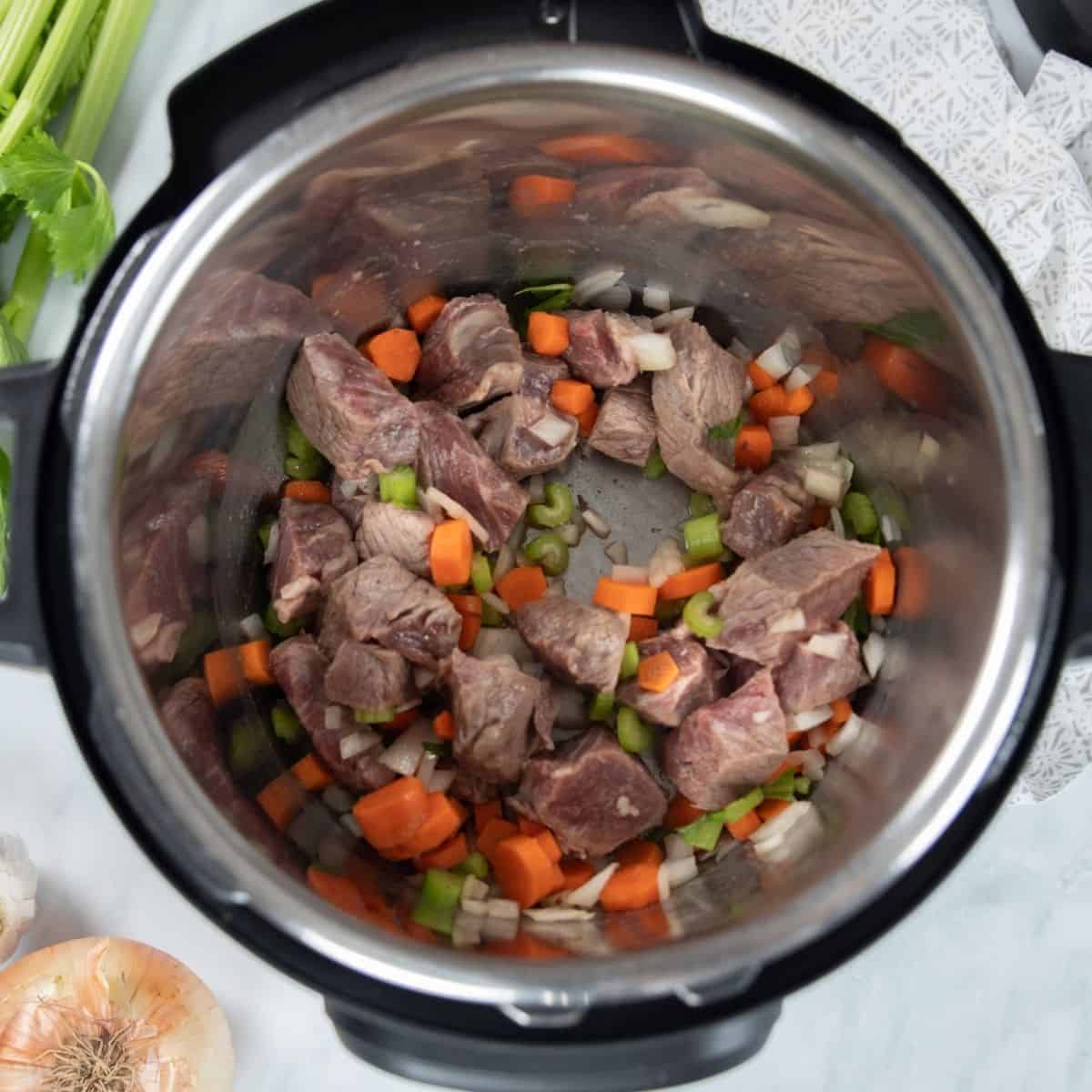 Beef, onions, celery, and carrots sauteed in the inner pot of the instant pot.