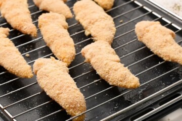 Chicken tenders breaded on baking rack.