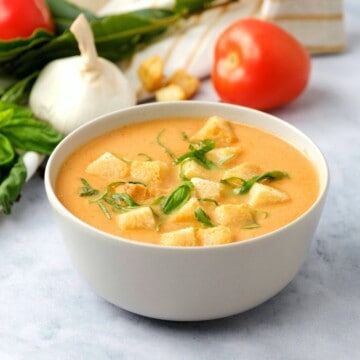 Bowl of creamy tomato soup topped with croutons and basil.
