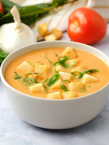 Bowl of creamy tomato soup topped with croutons and basil.