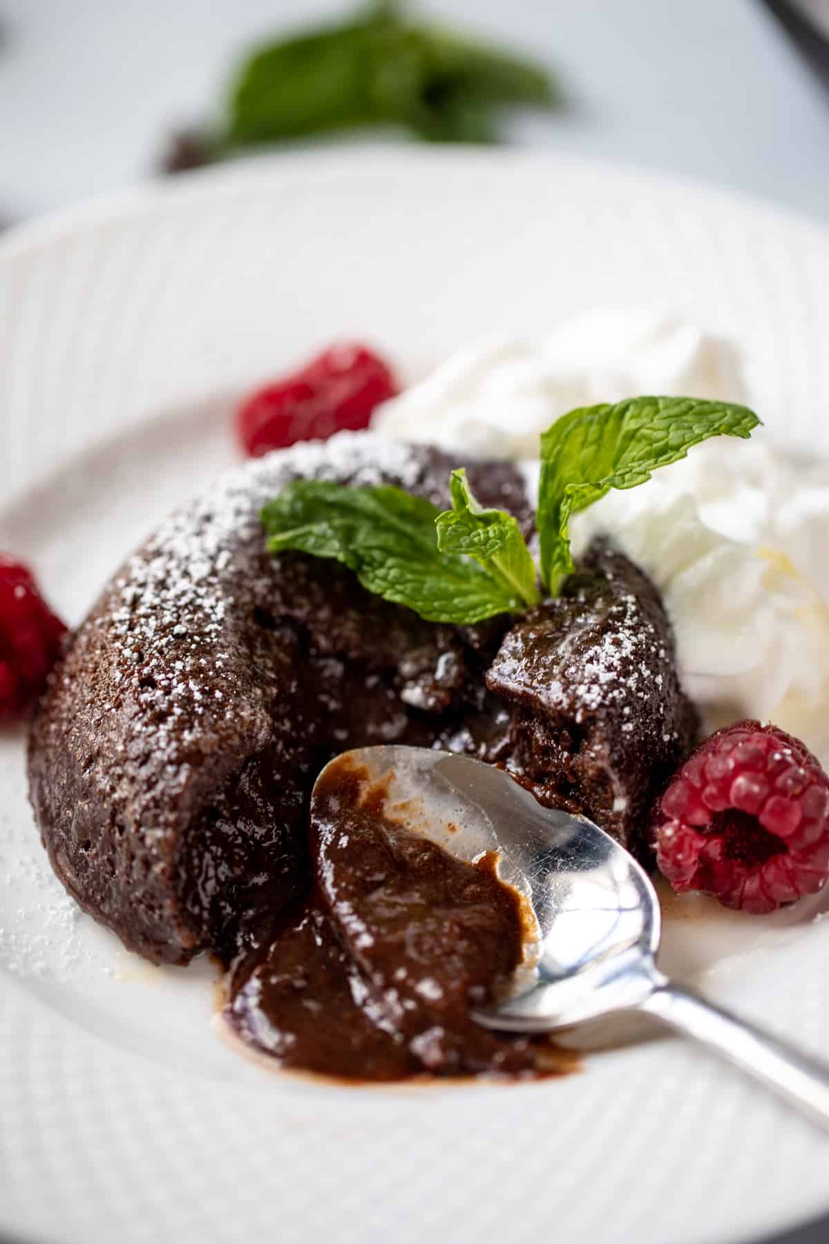 Chocolate lava cake on white plate with spoon cutting into it to show chocolate ooze. 