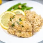 Instant Pot Lemon Chicken Thigh on a white plate next to brown rice.