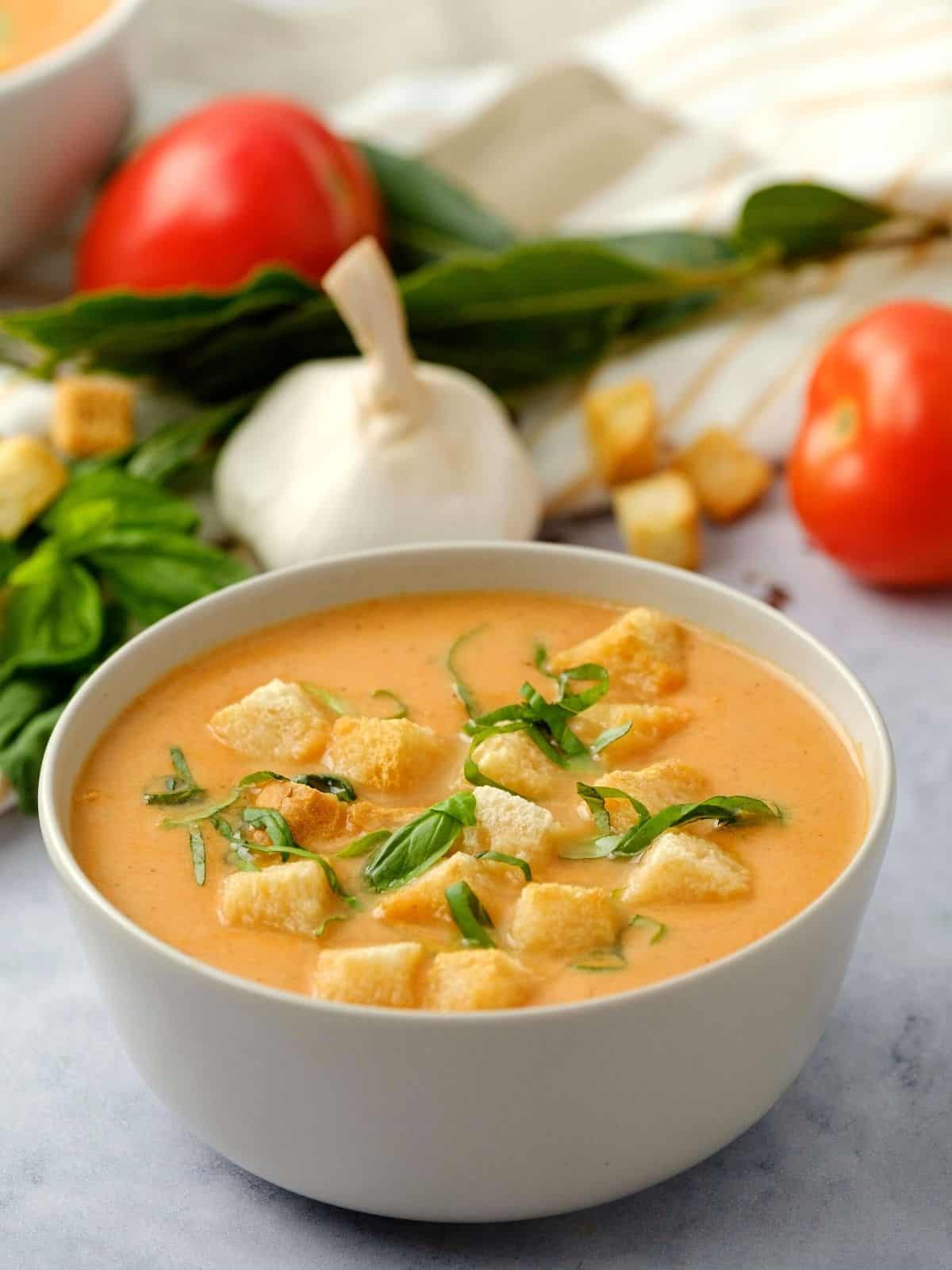 Bowl of creamy tomato soup topped with croutons and basil. 