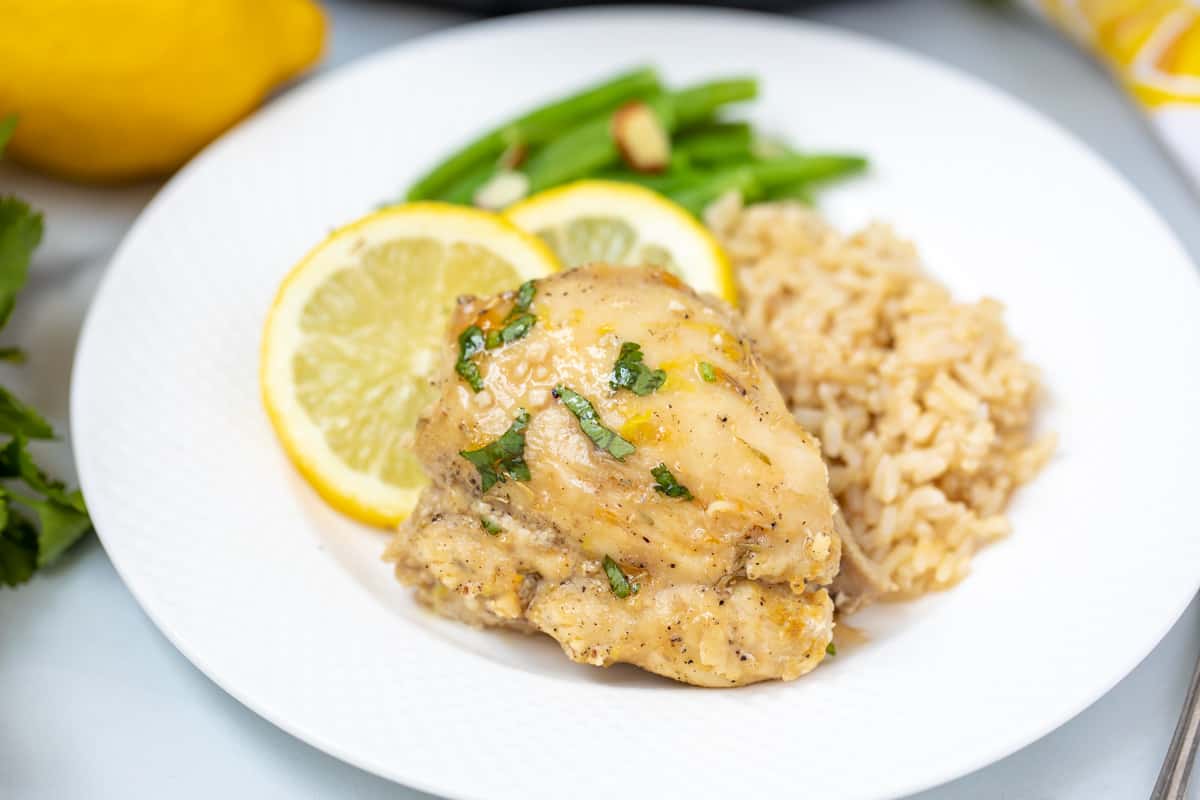 Instant Pot Lemon Chicken Thigh on a white plate next to brown rice. 
