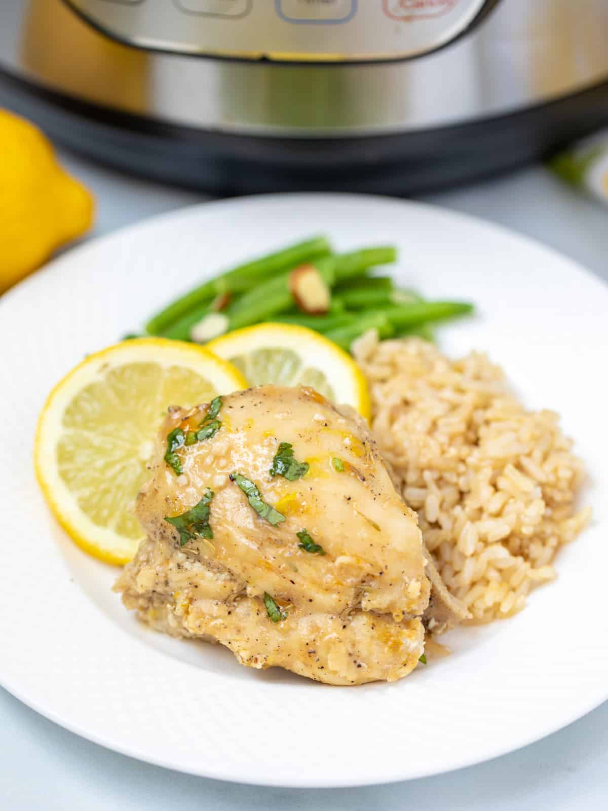 Lemon chicken on white plate with brown rice and green beans. 