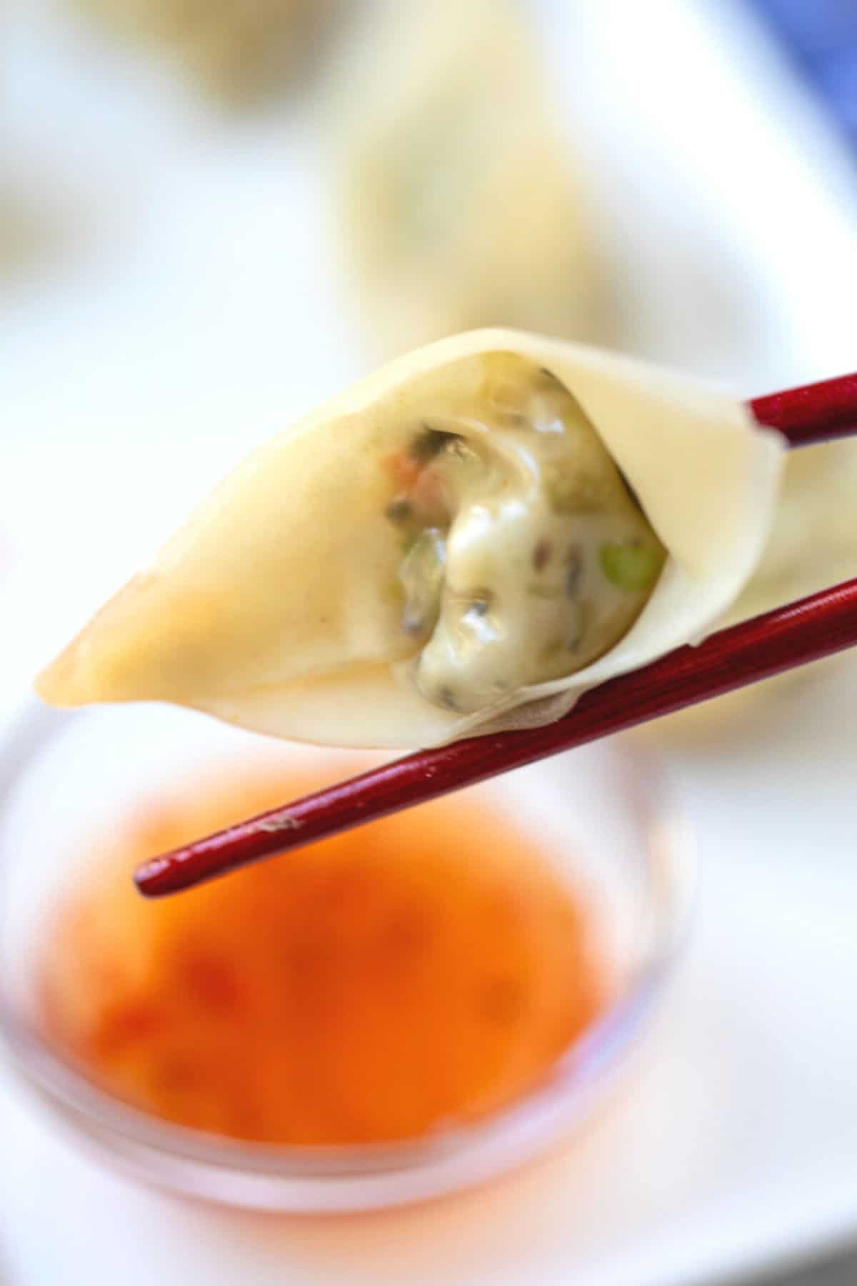 Potsticker on Wooden Chopsticks being dipped into sweet chili sauce. 