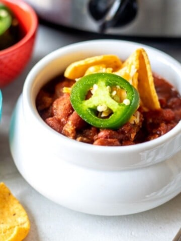 Bowl of chili with corn chips next to crockpot.