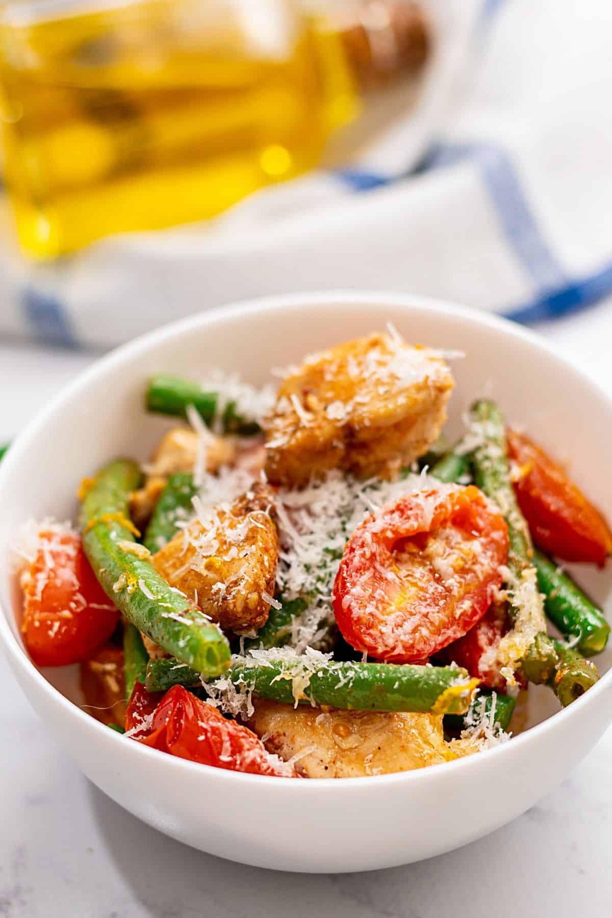 Chicken with green beans and tomatoes dished up in white bowl. 