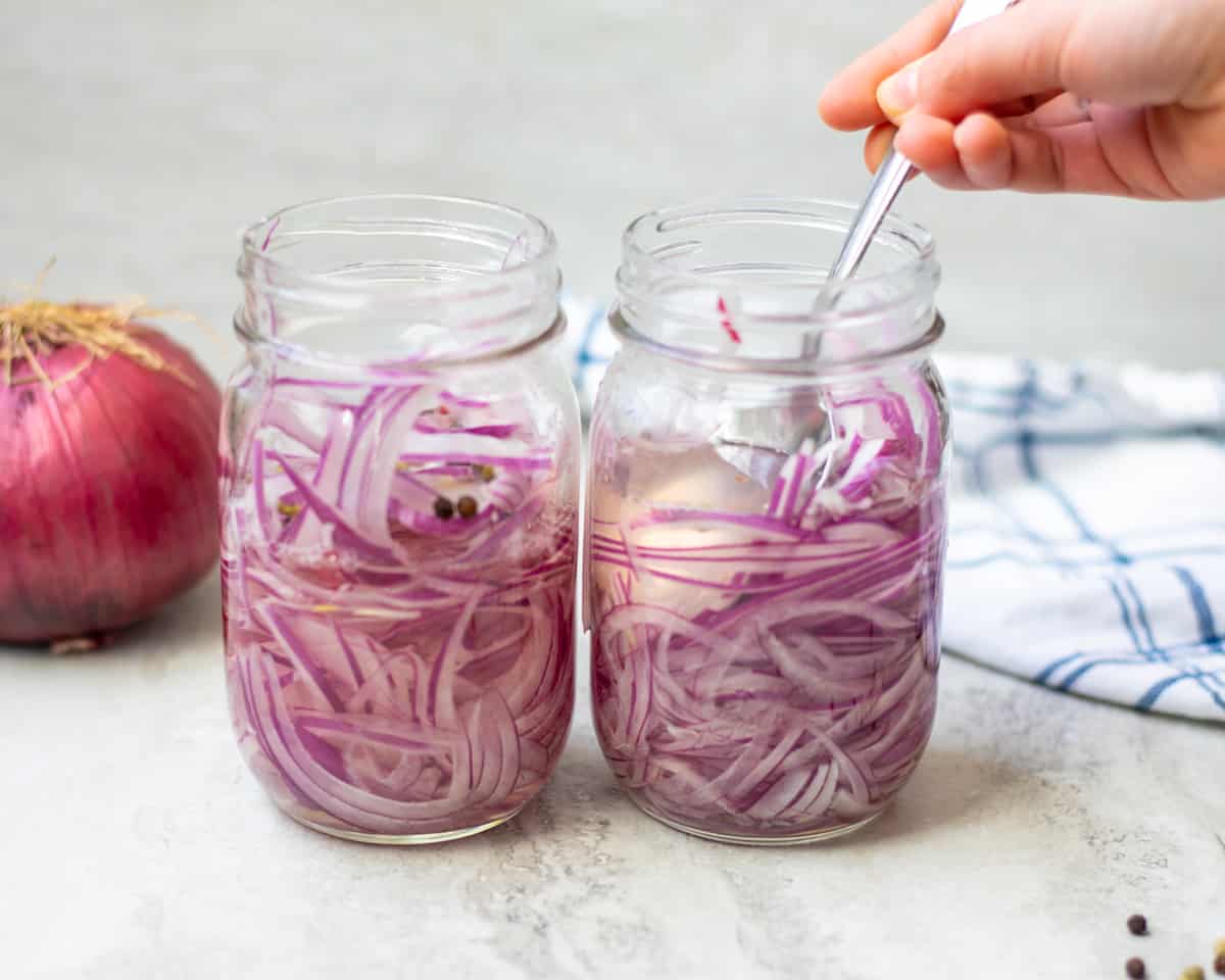 Spoon pushing down red onions in pickling liquid. 