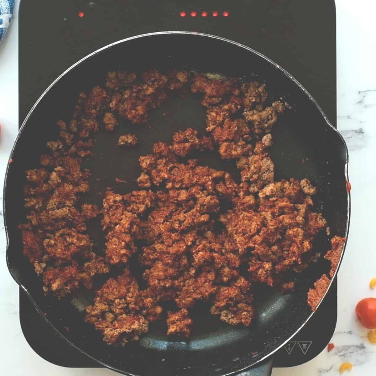 Ground beef with tomato paste and spices in a skillet.