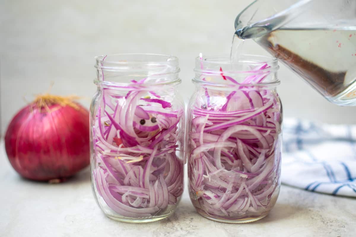 Pouring pickling liquid in 2 jars of sliced red onions.