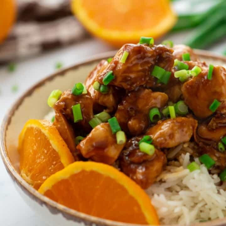 Bowl of orange chicken on top of rice.