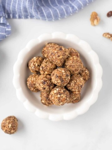 Oatmeal Balls stacked in white bowl next to walnuts and dates.