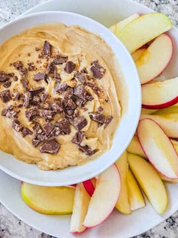 Cream Cheese Apple Dip in white dish topped with chopped toffee bar and served with sliced apples on the side.