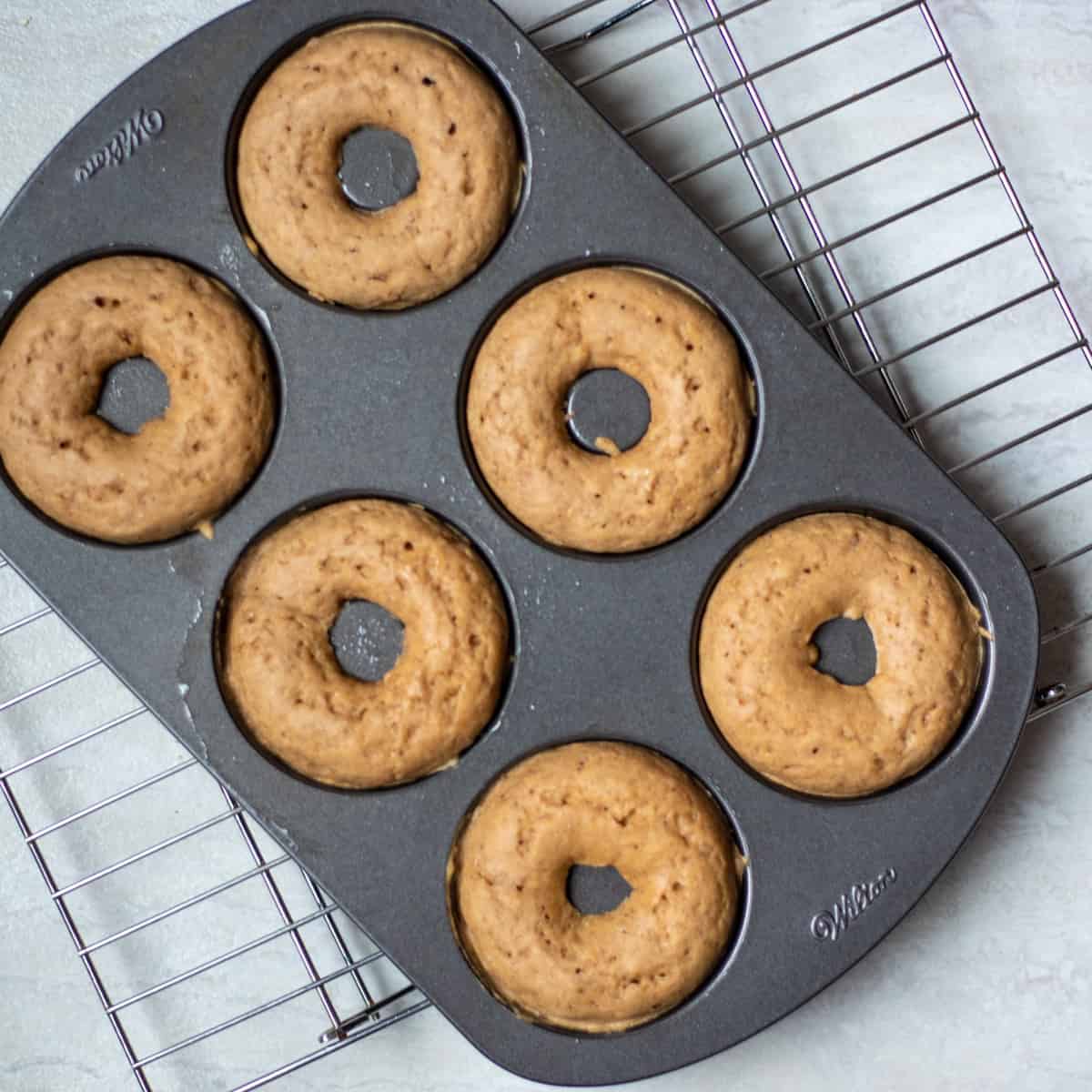 Baked donuts in donut pan cooling on cooling rack. 
