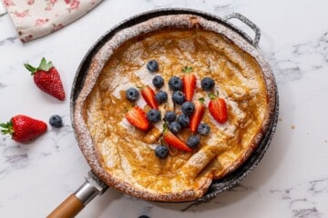 Baked Dutch oven pancake in skillet with berries and maple syrup.