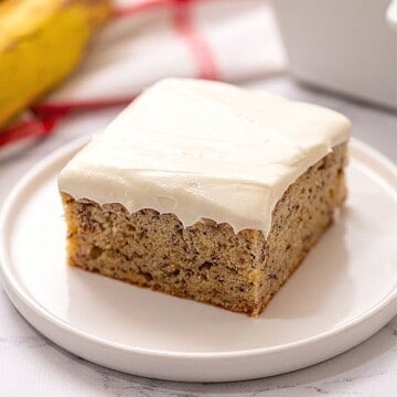 Slice of banana cake with cream cheese frosting on a white plate.