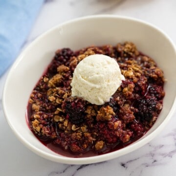 Bowl of blackberry crisp with scoop of vanilla ice cream in white bowl.