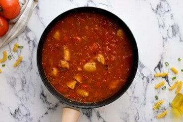 Skillet with chicken, broth, and diced tomatoes.
